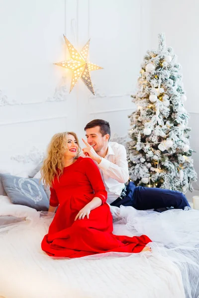 Milující pár šťastně usmíval na lůžku u vánočního stromu — Stock fotografie
