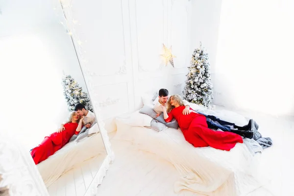 Το νεαρό ζευγάρι που στηρίζεται στο κρεβάτι κοντά στο χριστουγεννιάτικο δέντρο — Φωτογραφία Αρχείου