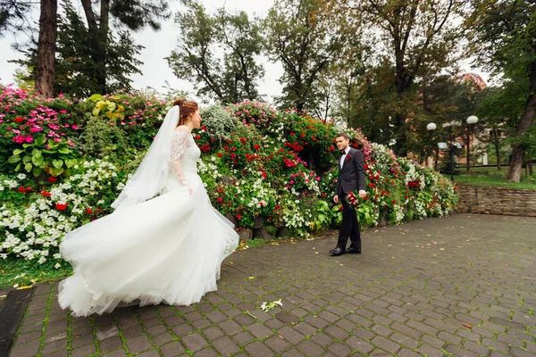 La novia en un hermoso vestido blanco corre a su marido sosteniendo —  Fotos de Stock