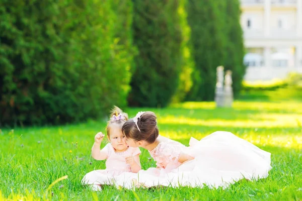 De oudere zus kussen de jongere zus, zittend op het gras — Stockfoto