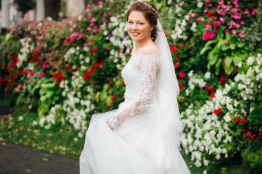 Renkli çiçeklerin arka planında büyüleyici bir gelinlik içinde gülümseyen gelin.