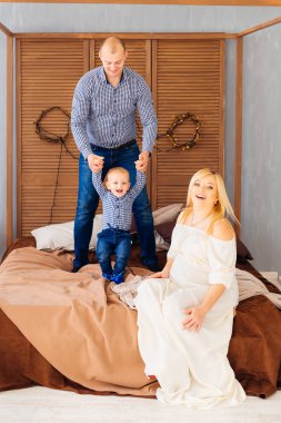 Baba ve oğul yatakta ve hamile atlama oturmuş ve gülümseyen anne