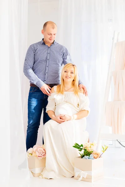 Mąż stoi obok żony w ciąży, który siedzi na krześle — Zdjęcie stockowe
