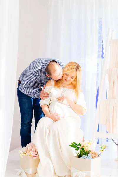 Um marido beija suavemente sua esposa grávida que se senta em uma cadeira e — Fotografia de Stock