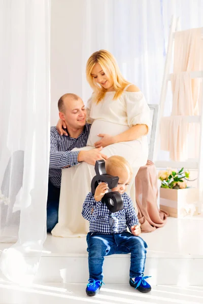 一个男人坐在一个怀孕的妻子旁边 他穿着一件漂亮的白色连衣裙 和一个玩玩具的小男孩 — 图库照片