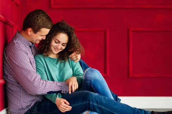 Abrazos sensuales de una pareja sentada en el suelo cerca de la pared roja —  Fotos de Stock