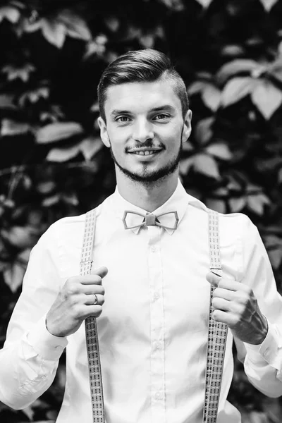 smiling guy in a shirt with suspenders on a background of leaves on the black and white photography which looks into the camera lens