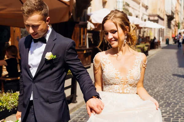 Newlyweds taking hands walking around a beautiful city on a beau — Stock Photo, Image