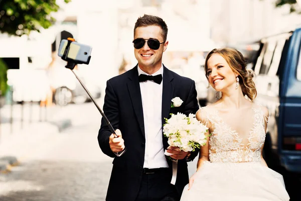 Egy elegáns vőlegény napszemüveg tart egy selfie bottal és vesz pi — Stock Fotó