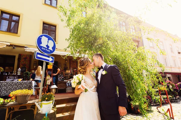 Новобрачные стоят возле кафе с украшениями и табличкой "Kiss pl. — стоковое фото