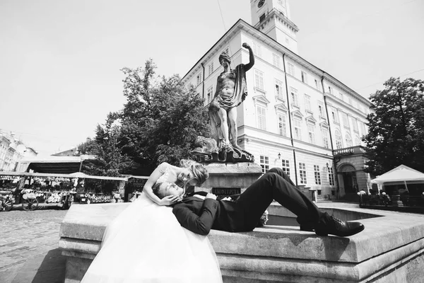 El novio acostado cerca de la novia sentado en la fuente y el s — Foto de Stock