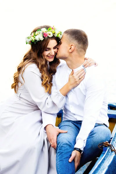 Um casal apaixonado sentado num barco. Uma rapariga com uma coroa de flores. — Fotografia de Stock