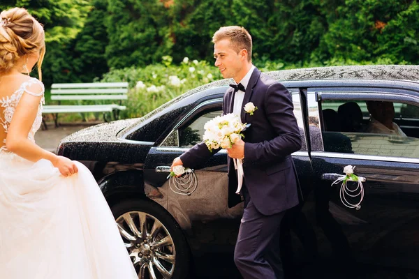 新郎在新娘门前打开一辆别致的黑色汽车。 — 图库照片