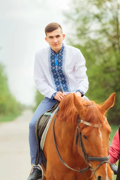 a pretty guy in an embroidered shirt sits in a saddle on a horse