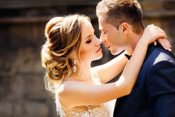 The bride hugs his groom around his neck and wants to kiss her