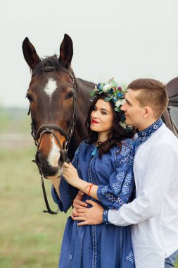 Kız güzel bir elbise ve kafasına bir çelenk ile a at başlığı için bir at tutar ve onun erkek arkadaşı ona bel hugs ve birlikte ata görünüyorlar