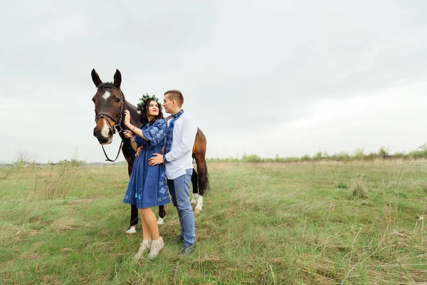 Um casal apaixonado fica no abraço e a menina segura um cavalo fo — Fotografia de Stock
