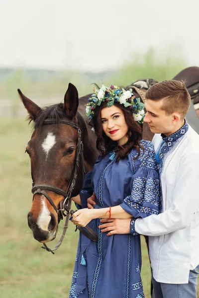 La fille dans une robe chic tient un cheval pour une bride et regarde — Photo