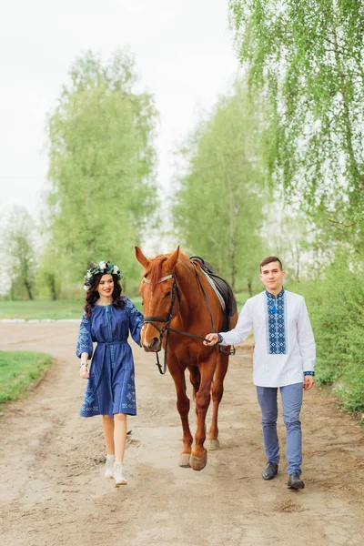 一个穿着节日服装的男孩和他的女朋友牵着一匹马当缰绳 开车送他走乡村小路 — 图库照片