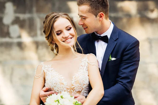 幸福的新娘在一个美丽的化妆白色礼服举行婚礼花束和一个新郎谁站在她旁边 — 图库照片