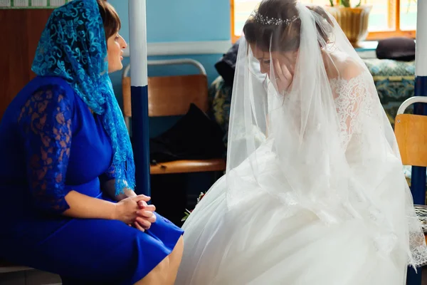 the bride in a gorgeous white dress cries before her wedding, and her mother calms her