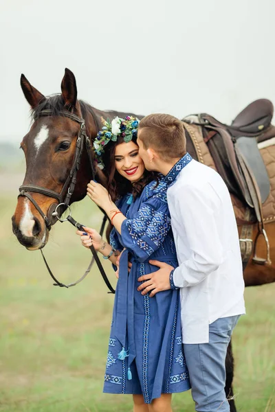 那个穿着漂亮衣服 头上戴着花圈的女孩抱着一匹马 男友吻了她的脸颊 — 图库照片