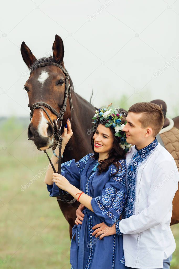 a couple in love in beautiful clothes is standing by the horse and admiring him