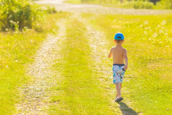 An einem schönen sonnigen Tag geht der Junge durch einen Feldweg mit — Stockfoto