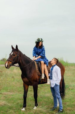 güzel bir kız zarif bir eyer bir at ve onun erkek arkadaşı işlemeli bir gömlek üzerinde oturan bir güzel elbiseler içinde onun yanında duruyor ve onlar birbirlerine bakıyorlar