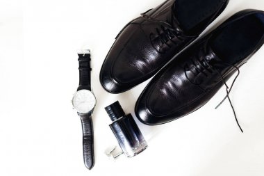 siyah erkek ayakkabıları, parfüm, kol düğmeleri ve beyaz arka planda şık saat