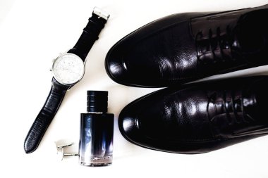 Beyaz bir arka plan üzerinde siyah erkek ayakkabı, parfüm, kol düğmeleri ve şık izle üstten görünüm