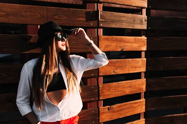 Das Mädchen hält ihre Hand auf einem schwarzen Hut und ihre Sonnenbrille auf dem Kopf — Stockfoto