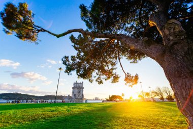 Lisbon, Portekiz - 28 Ocak 2018 nehir kıyısında bulunan bir yeşil çim akşam güneş parlar. belem Kulesi yakınındaki nehrin kıyısında yürüyen turist
