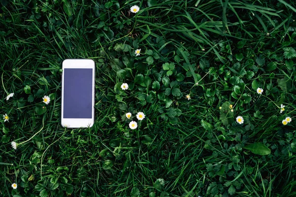 A white phone with a large screen is lying on the green grass