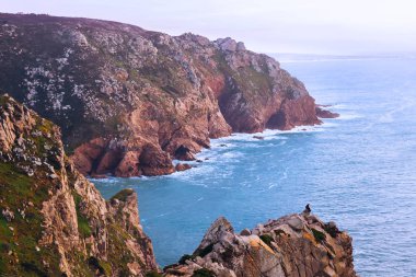 Kayalık bir tepe ve gün batımı hayran bir adam oturuyor. inanılmaz bir