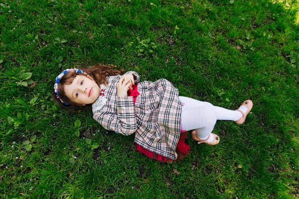 Una linda chica se acuesta en una hierba verde en un hermoso vestido y se ve — Foto de Stock