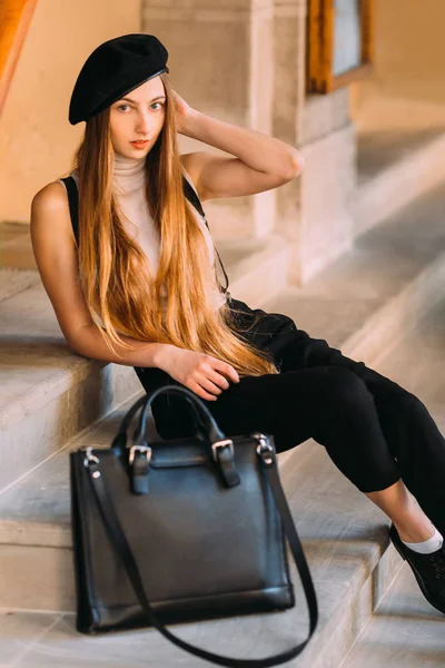 girl in black clothes and with long, beautiful hair sitting on the stairs of the house