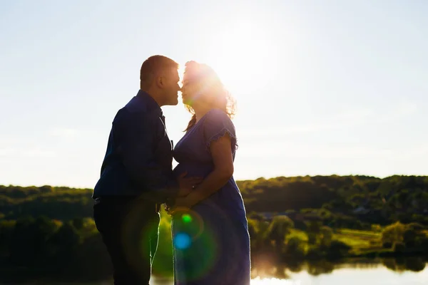 Een man kussen zijn zwangere vrouw op de achtergrond van een meertje — Stockfoto