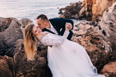 Yeni evliler okyanus manzaralı kayalık sahilde dans ediyorlar. güzel beyaz 