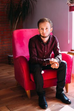 İş elbisesi giymiş genç bir adam koltukta oturuyor ve bakıyor. 