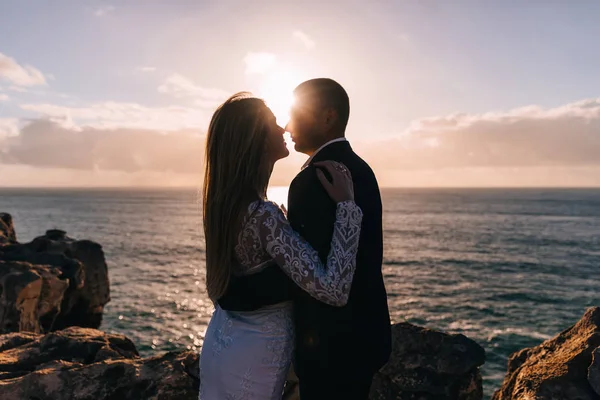 Brudgummen kramar bruden på den klippiga stranden och strålarna av — Stockfoto