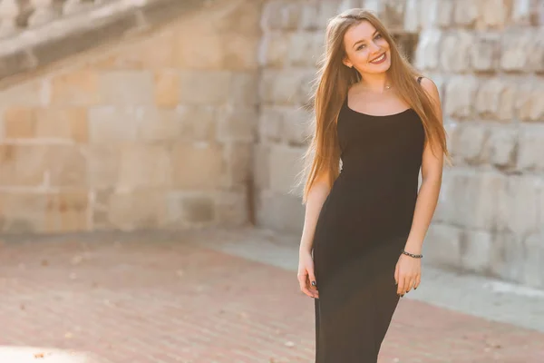 Chica en elegante vestido negro sonríe y mira a la cámara en la pared — Foto de Stock