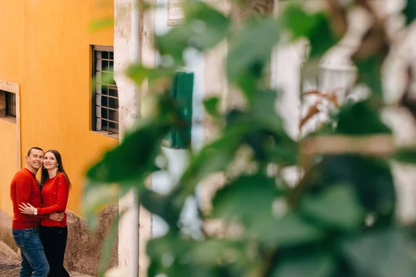 Pareja en suéteres rojos abrazándose y sonriendo cerca de la pared. borrosa br — Foto de Stock