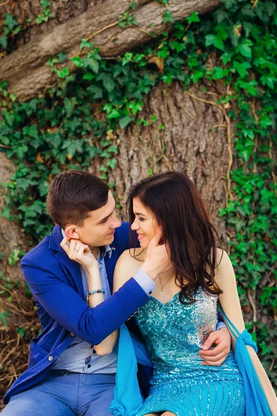 Couple amoureux en vêtements de fête s'asseoir près du tronc d'un arbre un — Photo