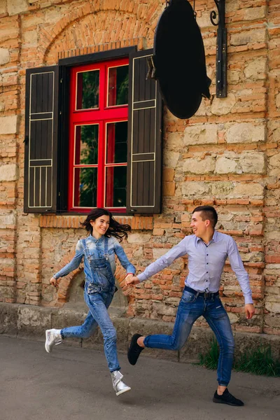 Το κορίτσι και ο τύπος κρατώντας τα χέρια και να τρέχει κοντά σε ένα κτίριο με — Φωτογραφία Αρχείου