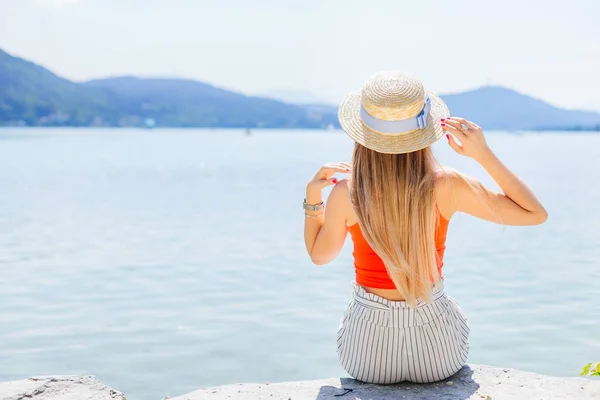 Dağ Gölü kıyısında oturan bir genç bayan. Hasır şapka ve uzun h — Stok fotoğraf