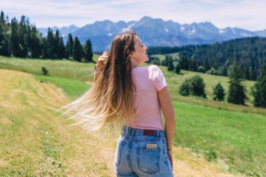 Kız uzun saçlarını sallıyor ve gözlerini kapatıyor. Meadow manzaralı