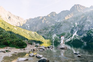 Birbirine aşık çiftler göl kenarındaki taşlara sarılıyorlar.