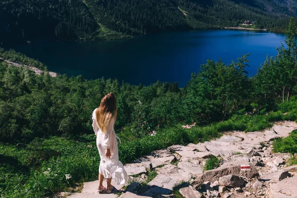 Beyaz elbiseli kız dönüyor. gölün kayalık kıyısı. Fikret — Stok fotoğraf