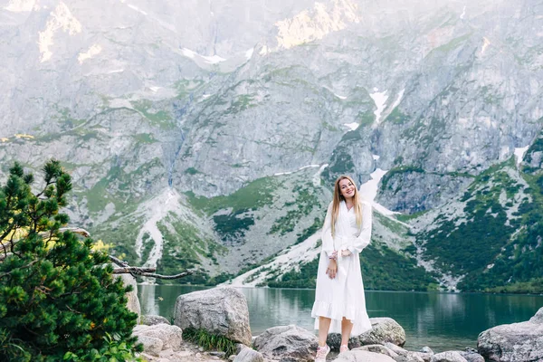 Jovem mulher na costa do lago de montanha em vestido branco. olhar para ca — Fotografia de Stock